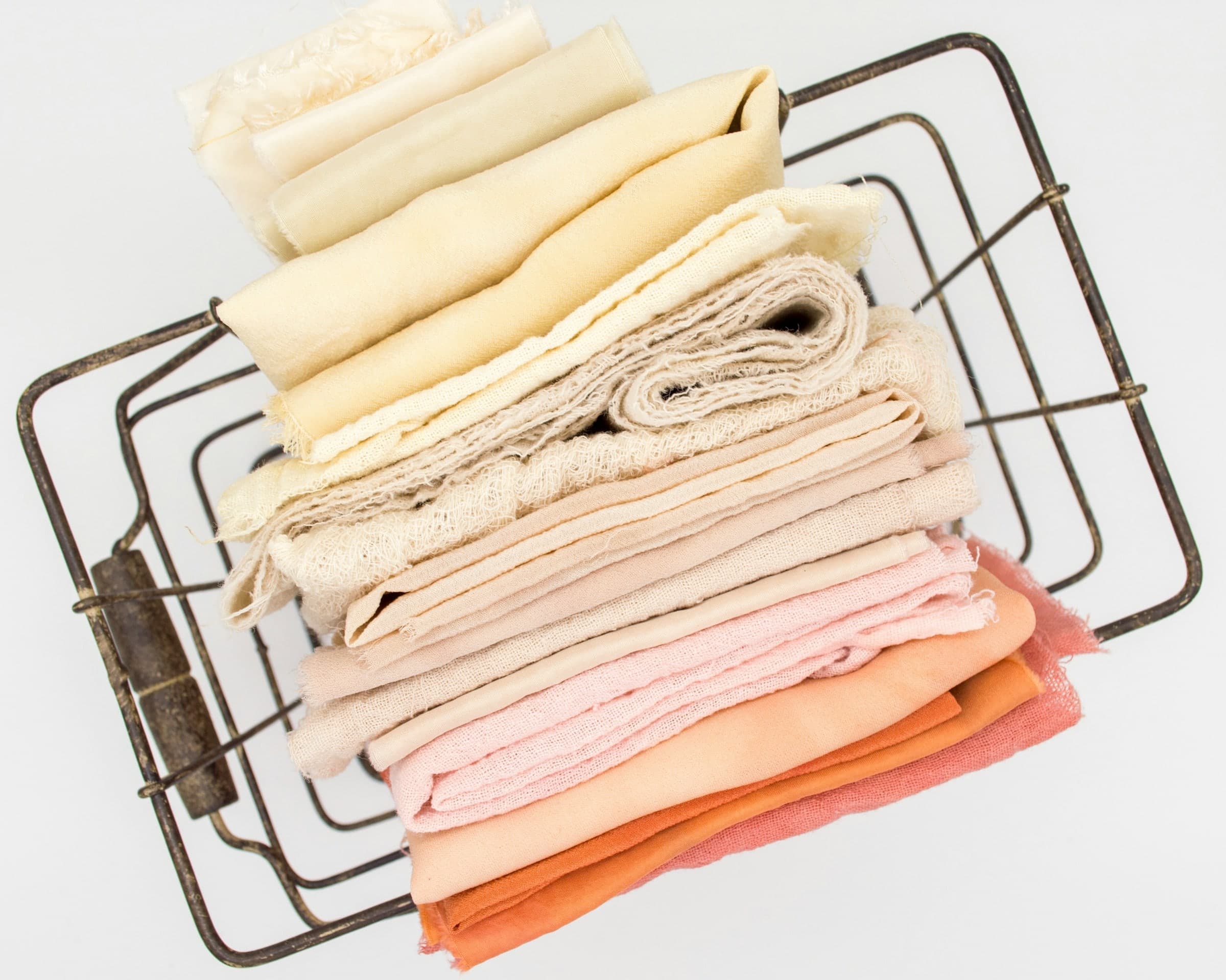 Une pile de linge plié, du blanc au rose et à l’orangé, dans un panier en fer.